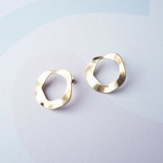Pair of gold hoop stud earrings with a cut out circular middle on a light grey background