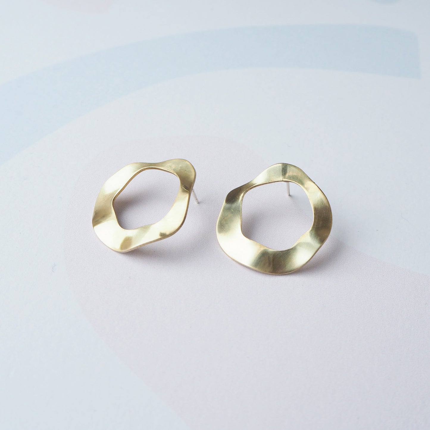 Pair of gold hoop stud earrings with a cut out circular middle on a light grey background