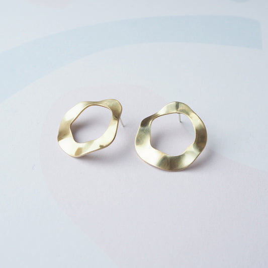 Pair of gold hoop stud earrings with a cut out circular middle on a light grey background