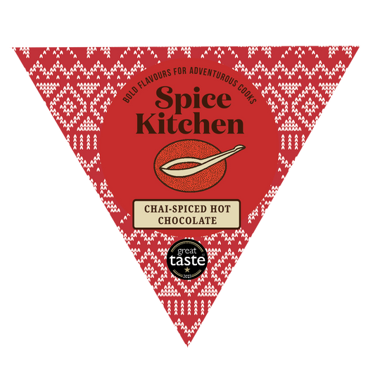 A red triangular Spice Kitchen product card for Chai-Spiced Hot Chocolate, featuring a white geometric pattern border, a central chocolate bowl illustration, and a Great Taste 2023 award badge at the bottom.