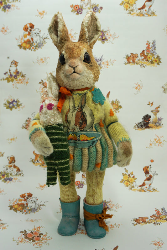 A plush rabbit doll stands upright, wearing a colourful knitted outfit with a rabbit motif. It holds a striped scarf and a small rabbit toy. The background features a whimsical pattern of animals and flowers. The rabbit wears blue boots with orange ribbon the right foot.