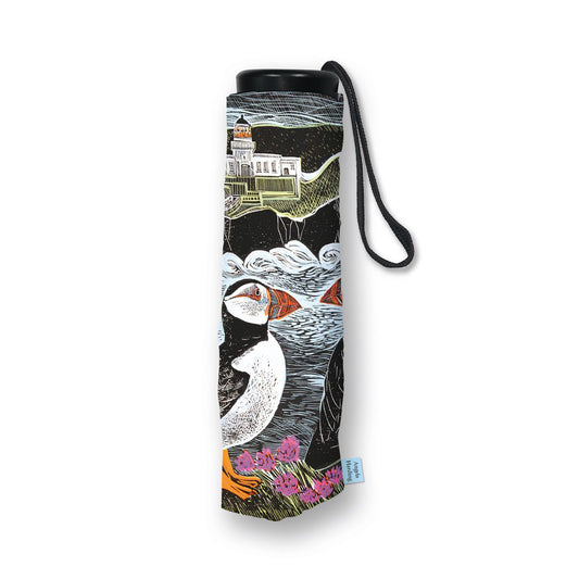 A rolled-up black umbrella with a wrist strap, featuring a detailed illustration of puffins, waves, and a lighthouse on the fabric. A small blue tag is visible at the bottom right.