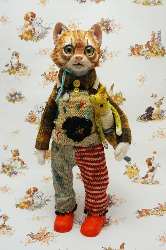 A whimsical cat doll stands upright, wearing a colourful knitted outfit with mismatched patterns and bright orange shoes. It holds a small yellow toy cat. The background features a playful animal-themed pattern.