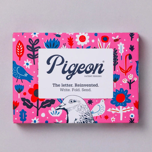 A vibrant pink box featuring a whimsical design of birds and flowers. The box is labelled "Pigeon" with the tagline "The letter. Reinvented. Write. Fold. Send." in bold lettering, suggesting a creative approach to letter writing.