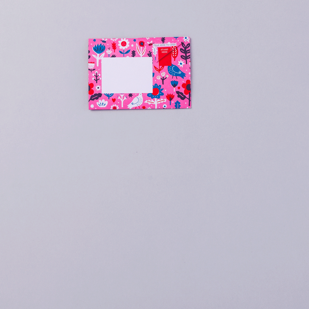 A vibrant pink sheet of paper with a floral pattern featuring various flowers and leaves in shades of red, blue, and white. The fabric is folded in a triangular shape, showcasing the intricate design against a light grey background.