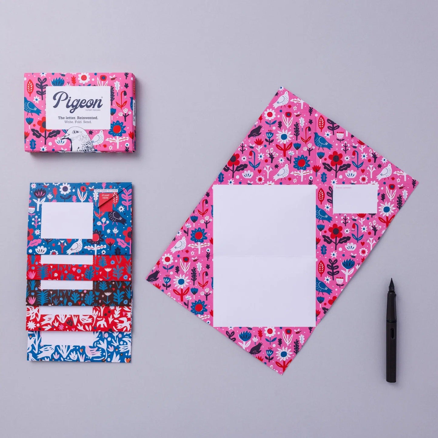 A flat lay of colourful stationery featuring a patterned letter set and matching envelopes. The letter set is predominantly pink with floral designs, while the envelopes are in blue and red patterns. A black pen is placed beside them.
