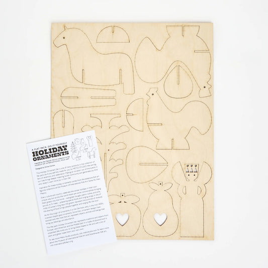 Wooden rectangular laser cut sheet of cut-out shapes on a white background next to an instruction sheet. The shapes include birds, horses, fruit and trees.