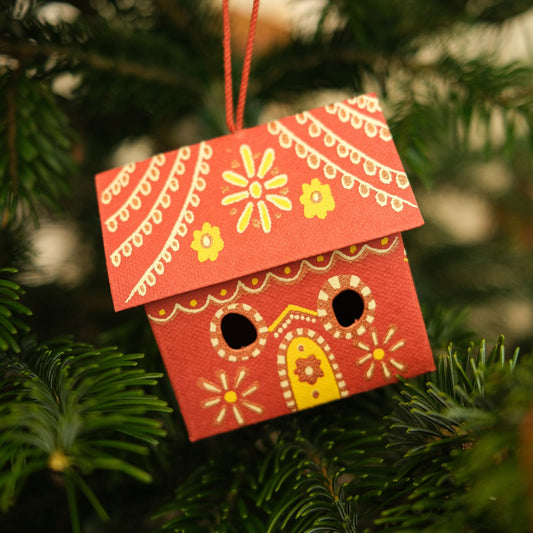 Decorative red gingerbread house ornament with yellow details hanging on a Christmas tree.