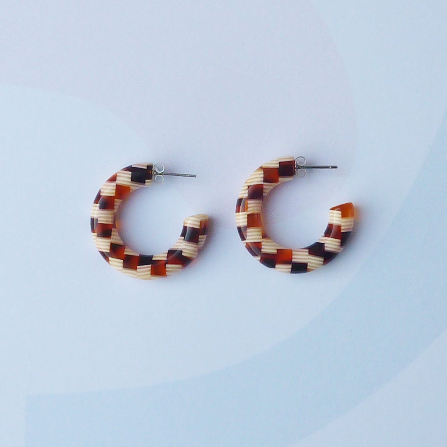 Pair of honey coloured larger checkered hoop earrings on a light blue background. 