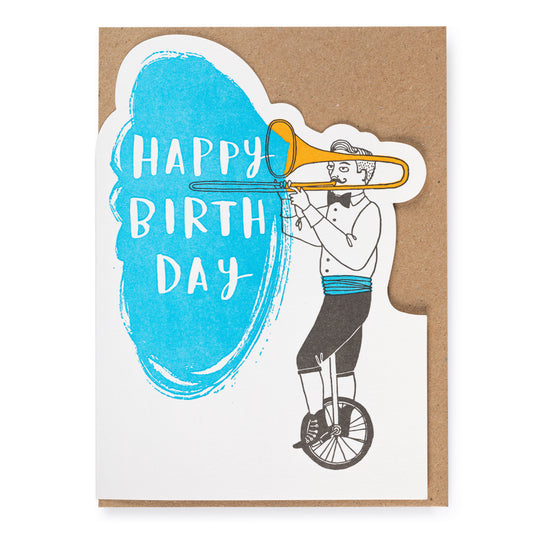 Birthday card with illustration of a person on a unicycle playing a trombone and 'Happy Birthday' text.