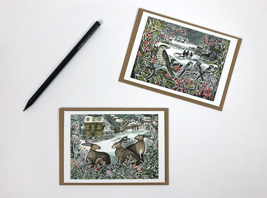 A pack of Christmas notecards featuring two original prints by Angela Harding. The prints feature wintry scenes with rabbits and birds. 