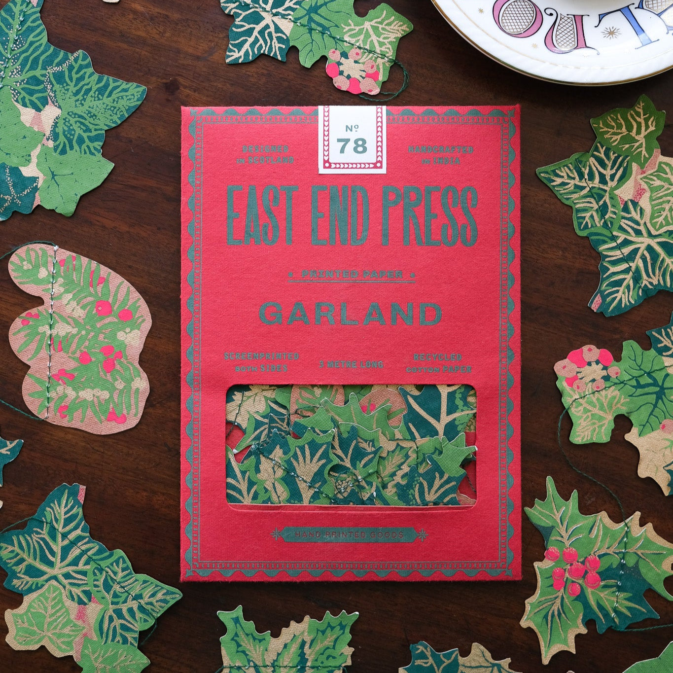 Packaging of East End Press Holly and Ivy Garland with decorative leaf designs on a wooden surface.