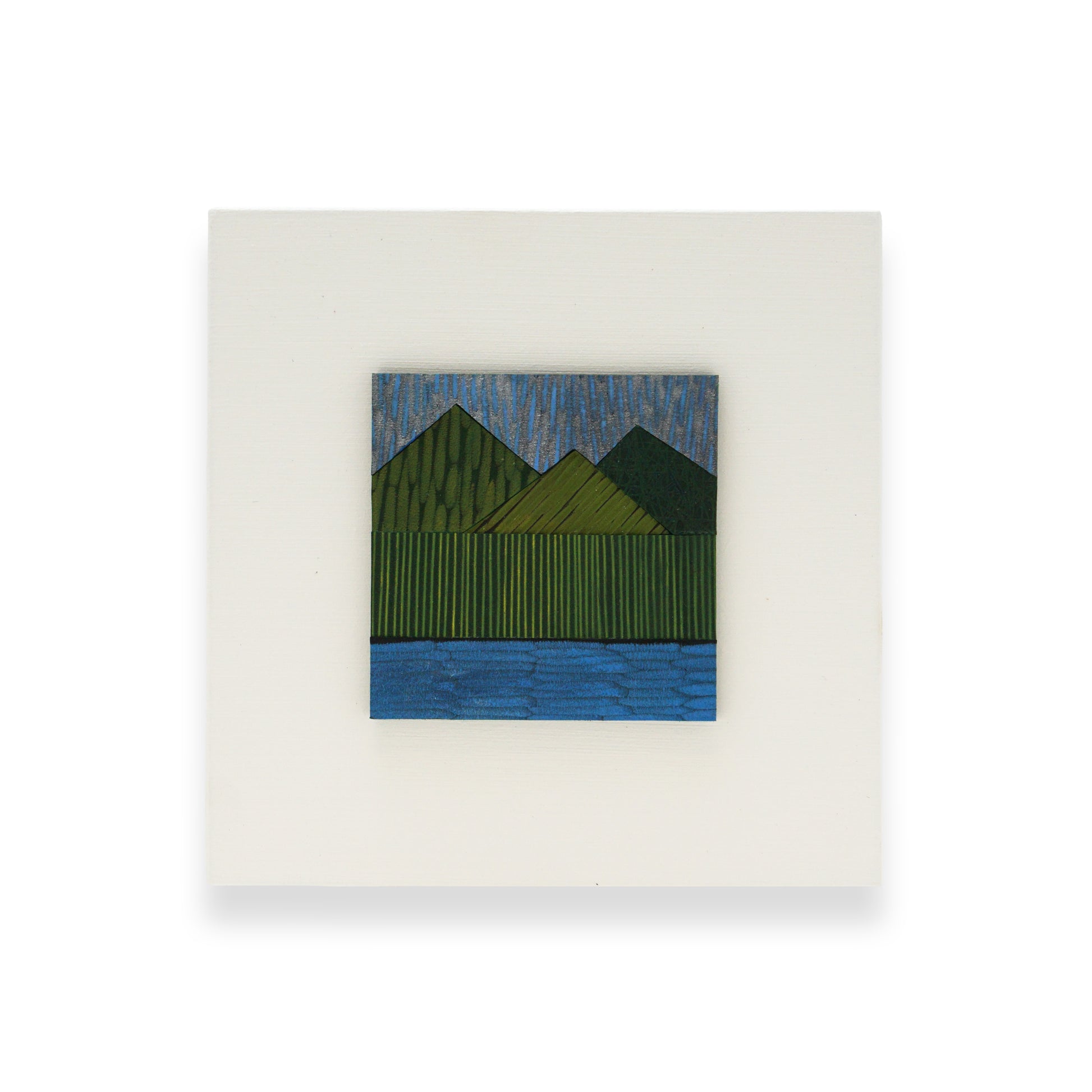 A leather collage mounted on a white MDF back. The collage depicts a landscape; green mountains and a blue body of water.