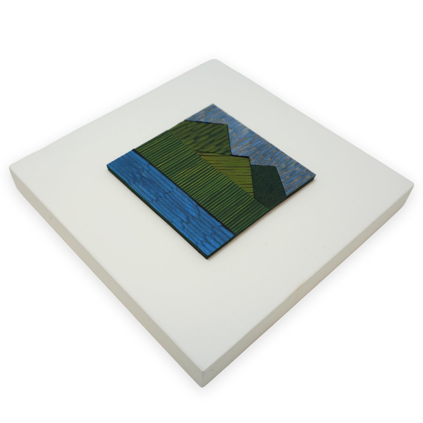 A leather collage mounted on a white MDF back. The collage depicts a landscape; green mountains and a blue body of water.