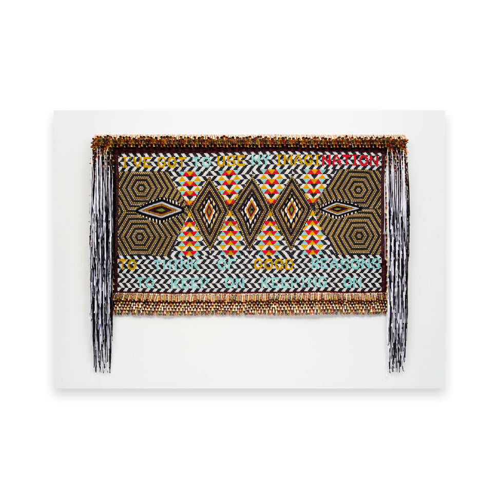 A vibrant textile artwork featuring geometric patterns in bold colours, including red, yellow, and black. The piece includes the text "I've got one imagination to good reason" woven into the design, framed with decorative fringes.