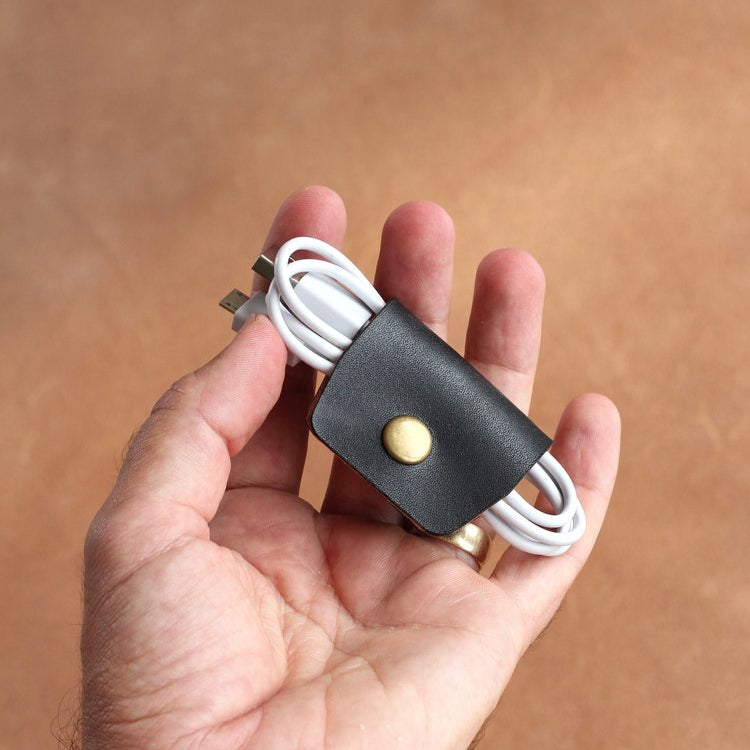 Hand holding a black leather cable wrap with a USB cable against a brown background