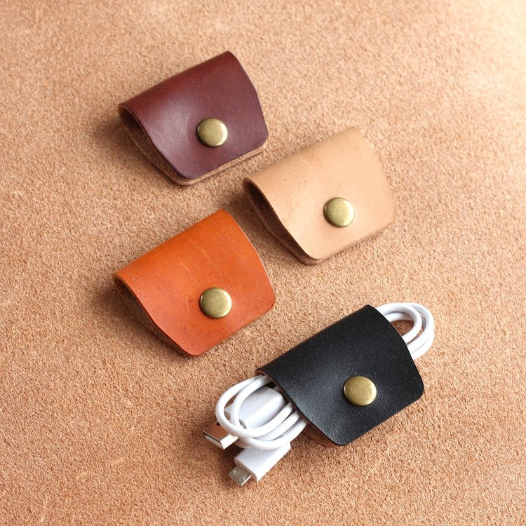 Four leather cable wraps in different colours with metallic poppers on a beige background.