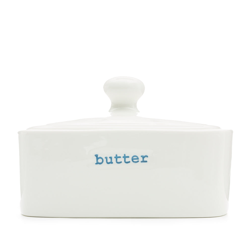 A white ceramic butter dish with the word 'butter' stamped in blue typewriter font on the side.