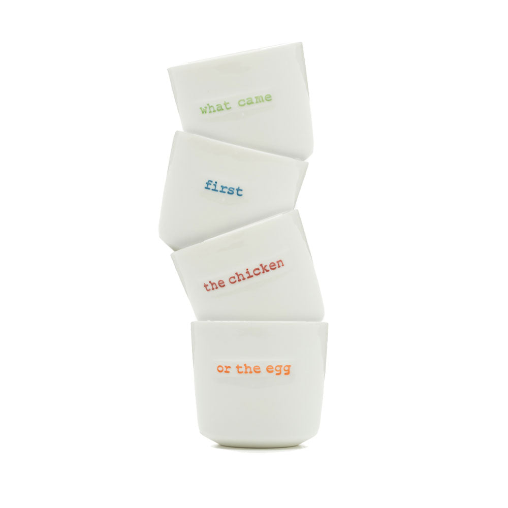 Stack of four white ceramic egg cups each with a different word stamped on the front