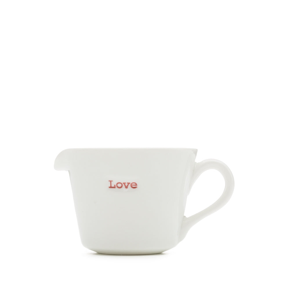 A white porcelain jug with the word 'love' written on it in red, having a pouring spout and handle.