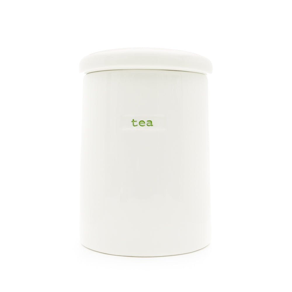 A white porcelain storage jar with the word 'tea' written on it in green, having a lid.