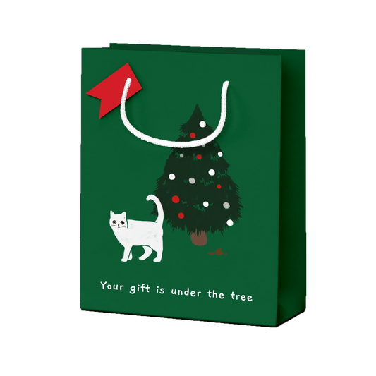 A green gift bag featuring a Christmas tree and a white cat. There appears to be a cat poo under the tree, plus the text 'your gift is under the tree'.