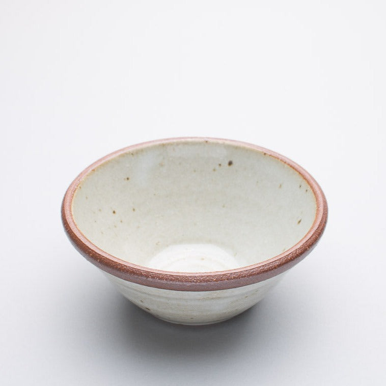 A small stoneware ceramic bowl with a cream hue and a dark brown rim.