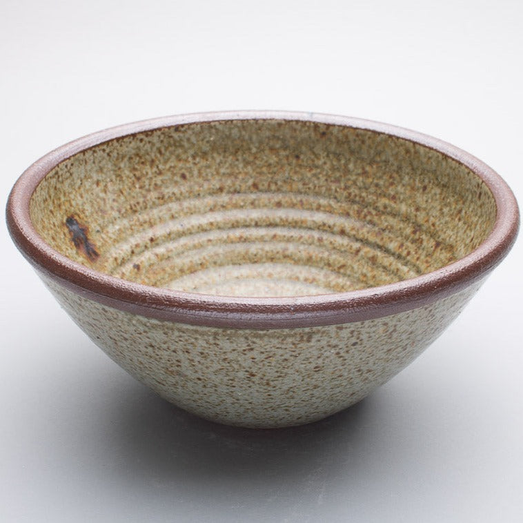 A large stoneware ceramic bowl with a beige and greenish hue and a dark brown rim.