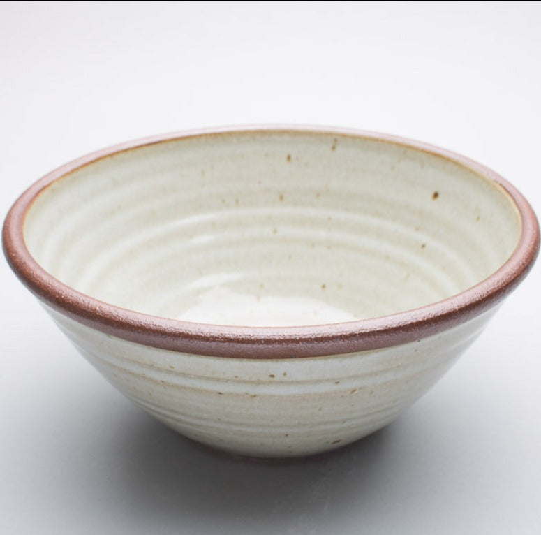 A large stoneware ceramic bowl with a cream hue and a dark brown rim.
