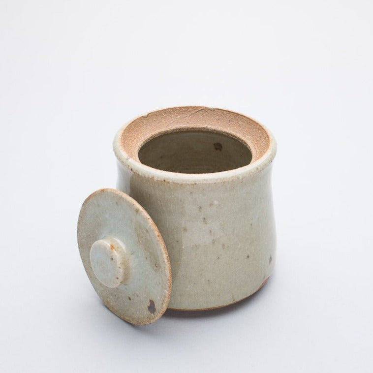 A beige ceramic honey jar with a lid, made of stoneware clay, with a creamy white glaze that may have a hint of blue.