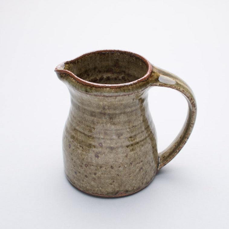 A small ceramic jug with a two-tone color, primarily a greenish hue with a darker brown at the rim and handle.
