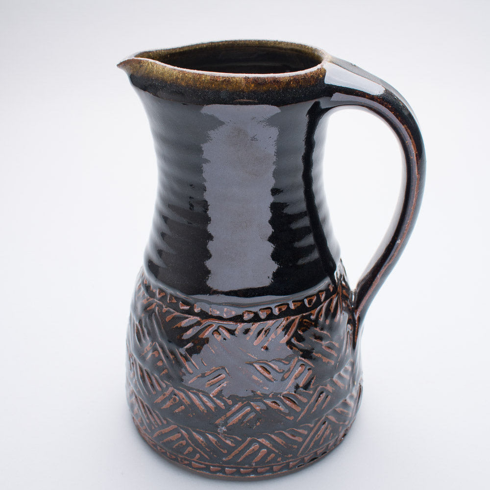 A large ceramic jug in shades of brown and black with textures in the glaze on the bottom half.