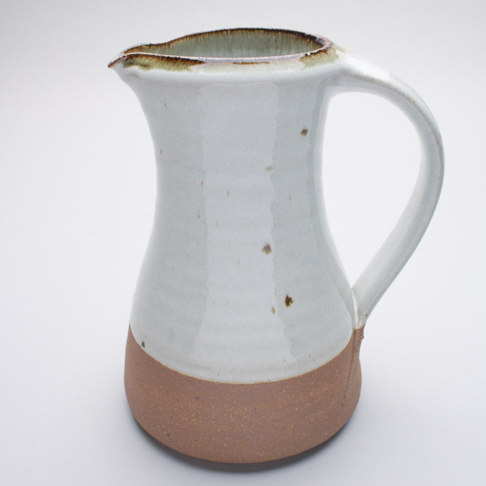 A large ceramic jug in a cream colour with a brown stripe at the base. Simple in shape and design.
