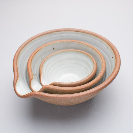 A set of three ceramic bowls stacked inside of each other. The bowls have three different sizes and featuring a pouring spout and a brown outer with a blue/white inside.