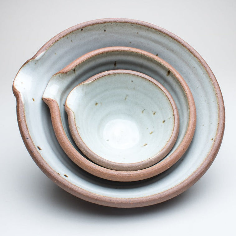 A set of three ceramic bowls stacked inside of each other. The bowls have three different sizes and featuring a pouring spout and a brown outer with a blue/white inside.