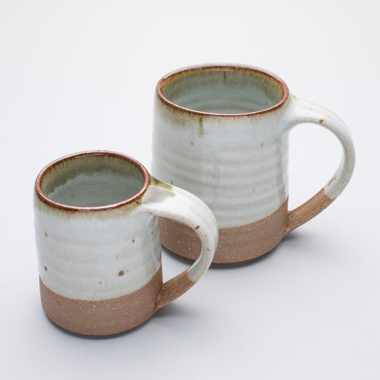 Two ceramic mugs with a speckled cream and brown finish, one larger and one smaller, both with handles.