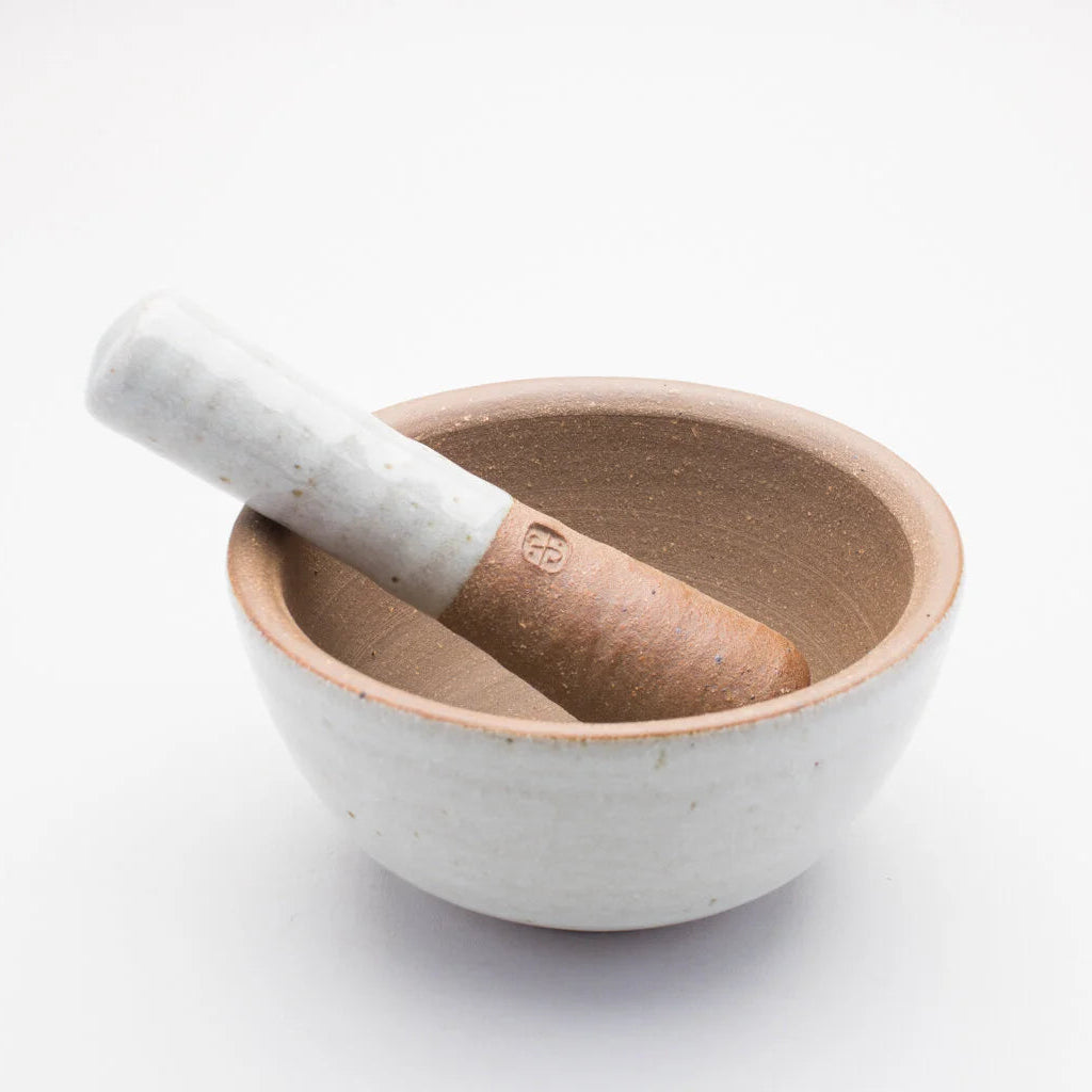 A ceramic pestle and mortar. The inside of the mortar is a textured brown, while the outer of mortar and handle of the pestle is a smooth cream/grey colour.