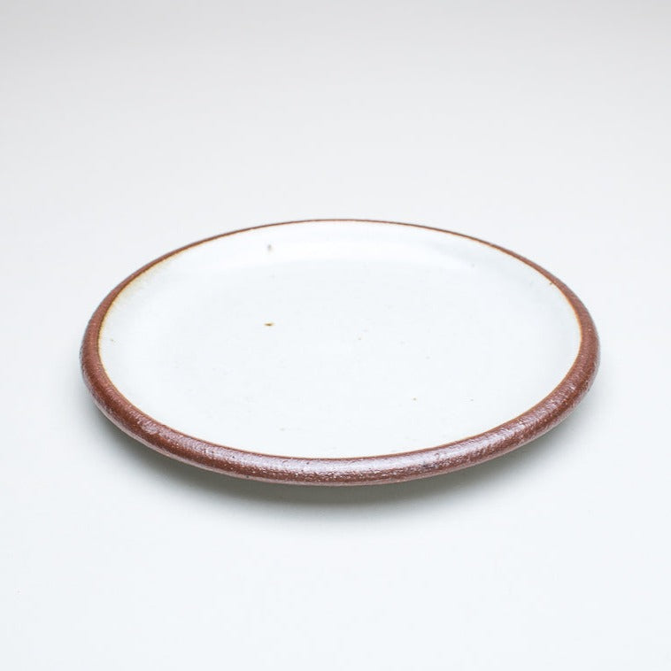 A ceramic plate with a cream centre and a greenish-brown rim, with variations in the glaze that give it a unique texture.