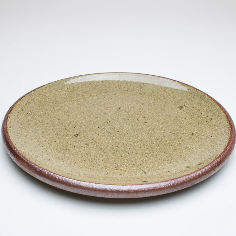 A ceramic plate with a green centre and a greenish-brown rim, with variations in the glaze that give it a unique texture.