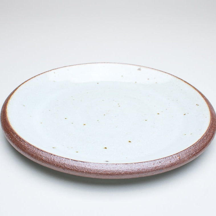 A ceramic plate with a cream centre and a greenish-brown rim, with variations in the glaze that give it a unique texture.