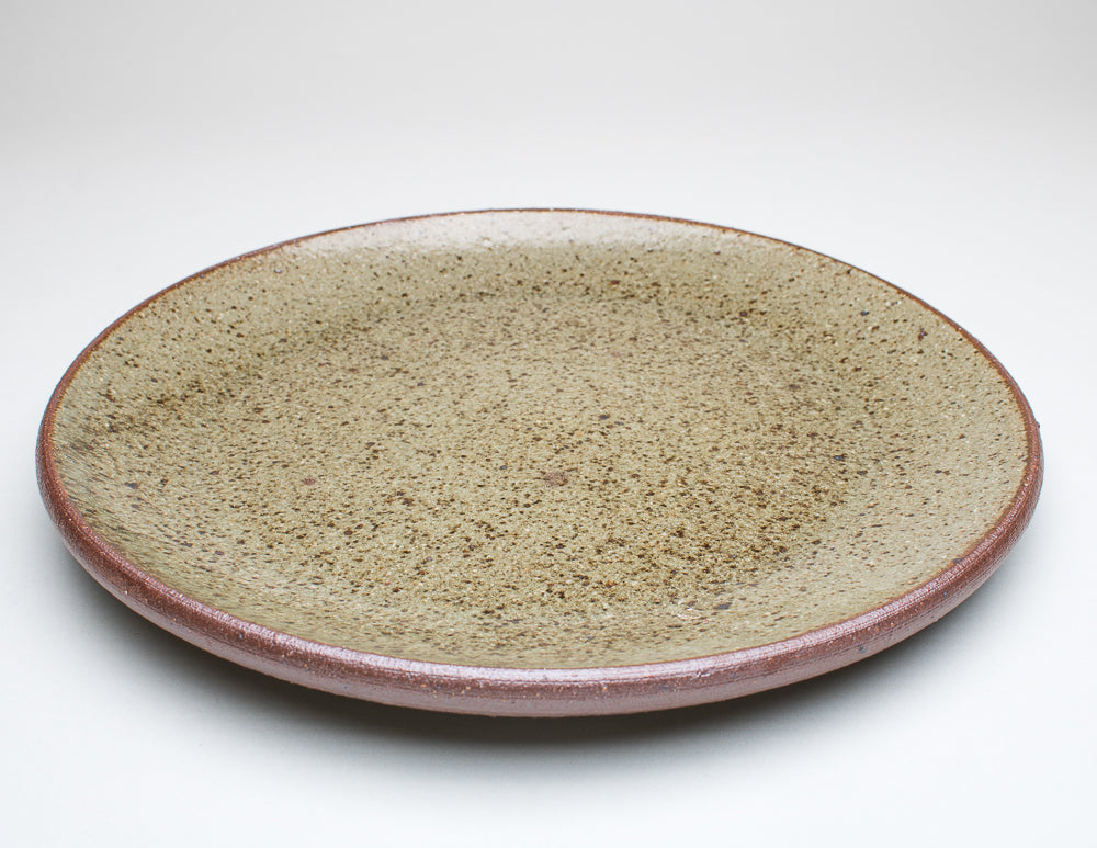 A ceramic plate with a green centre and a greenish-brown rim, with variations in the glaze that give it a unique texture.