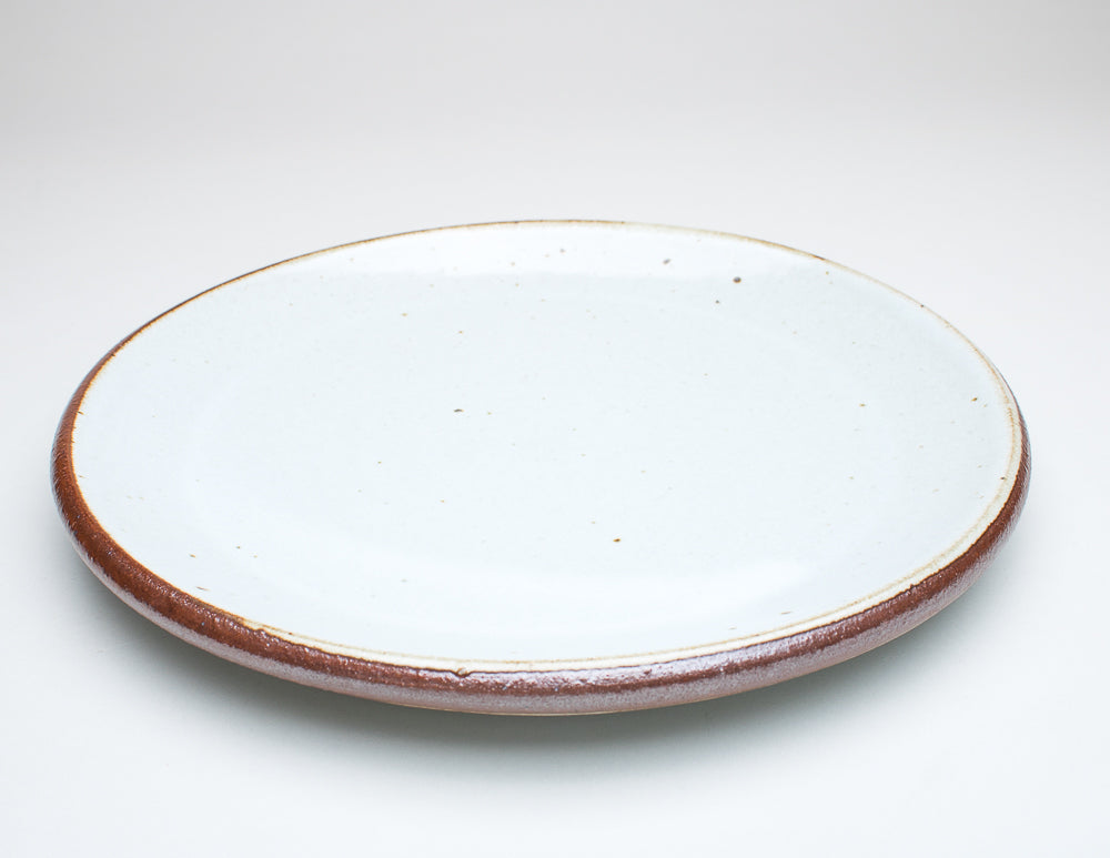A ceramic plate with a cream centre and a greenish-brown rim, with variations in the glaze that give it a unique texture.