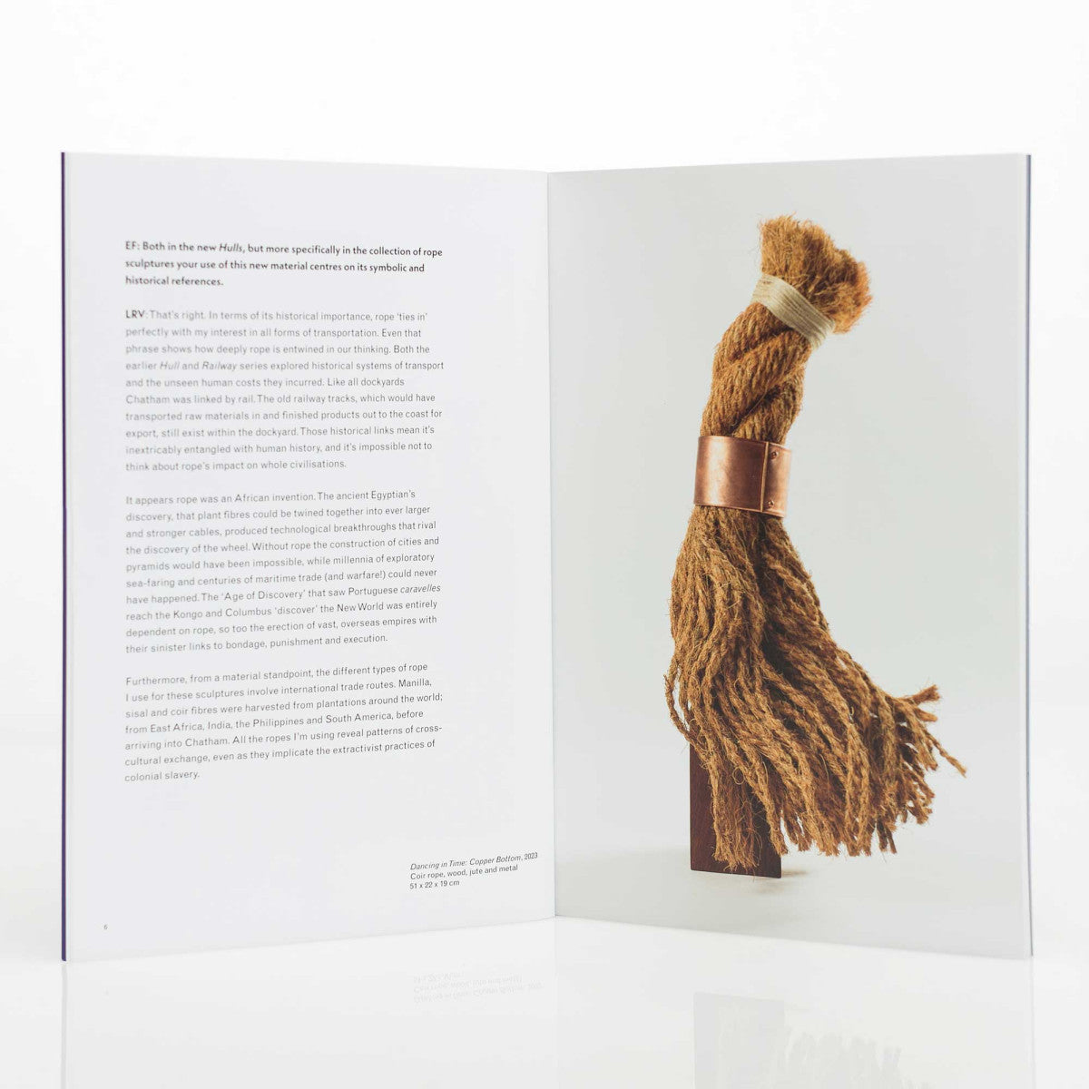 Book open to a page with text and an image of a rope sculpture on a wooden stand.