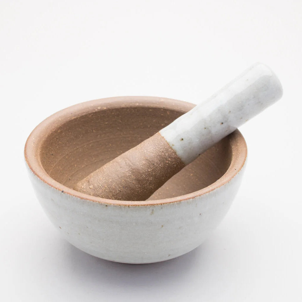 A ceramic pestle and mortar. The inside of the mortar is a textured brown, while the outer of mortar and handle of the pestle is a smooth cream/grey colour.