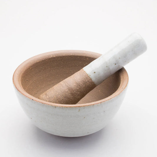 A ceramic pestle and mortar. The inside of the mortar is a textured brown, while the outer of mortar and handle of the pestle is a smooth cream/grey colour.