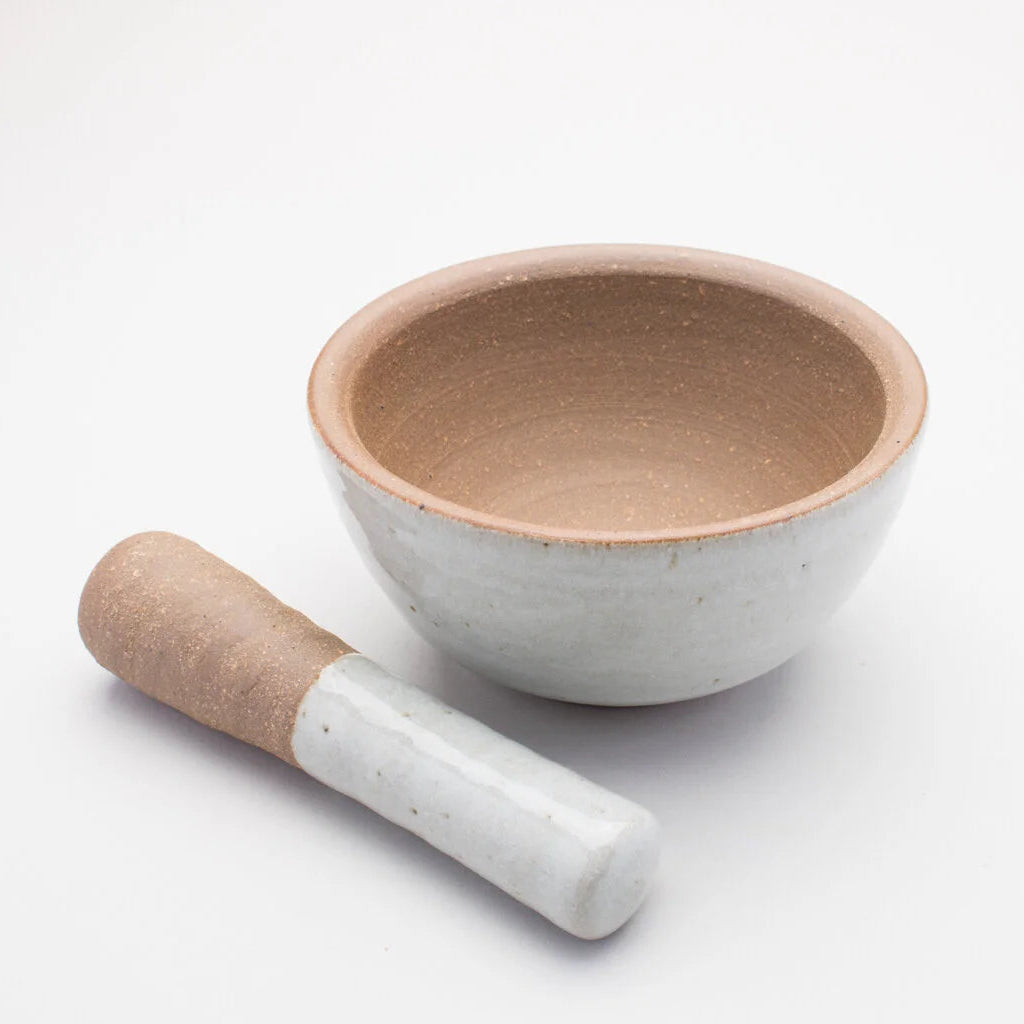 A ceramic pestle and mortar. The inside of the mortar is a textured brown, while the outer of mortar and handle of the pestle is a smooth cream/grey colour.