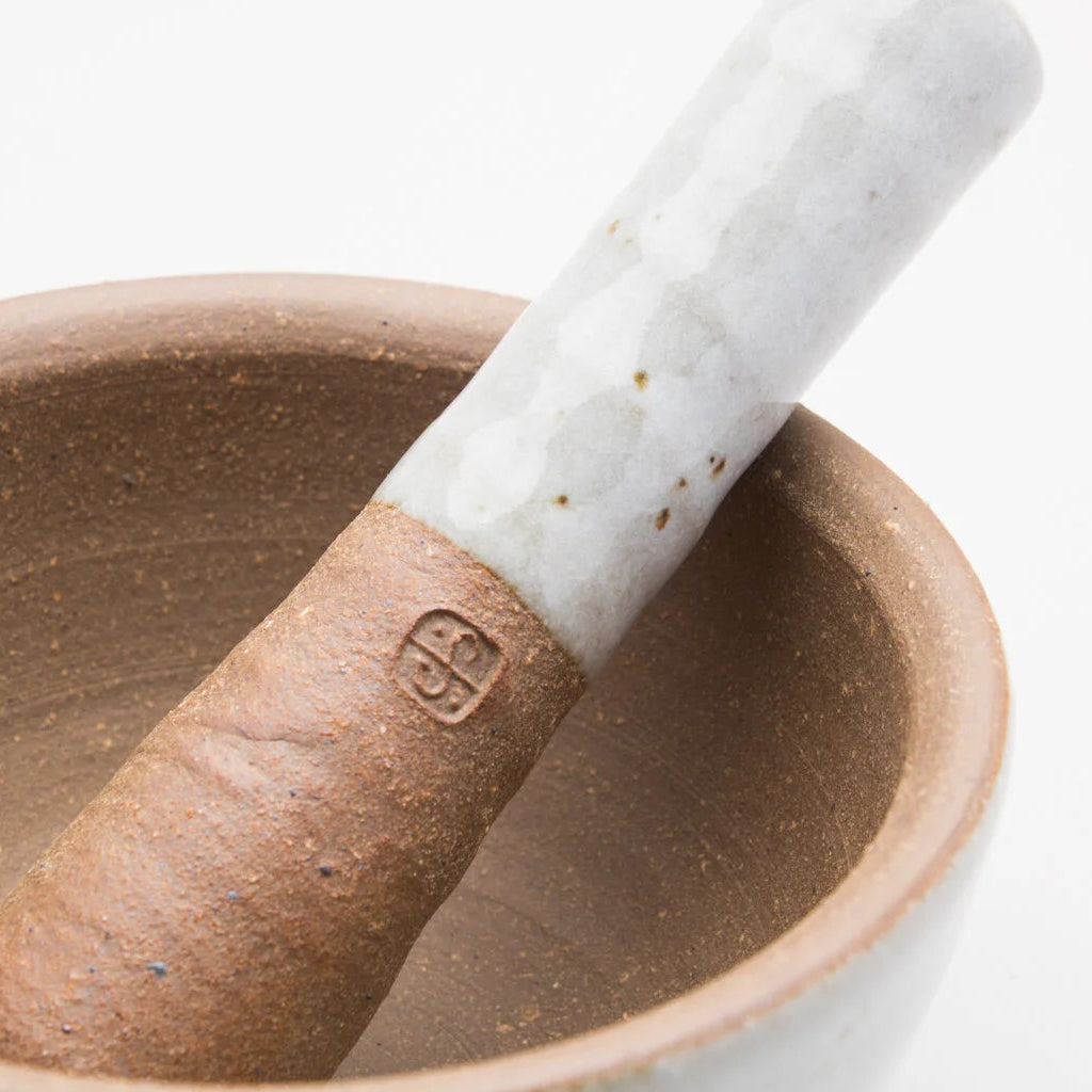 A ceramic pestle and mortar. The inside of the mortar is a textured brown, while the outer of mortar and handle of the pestle is a smooth cream/grey colour.
