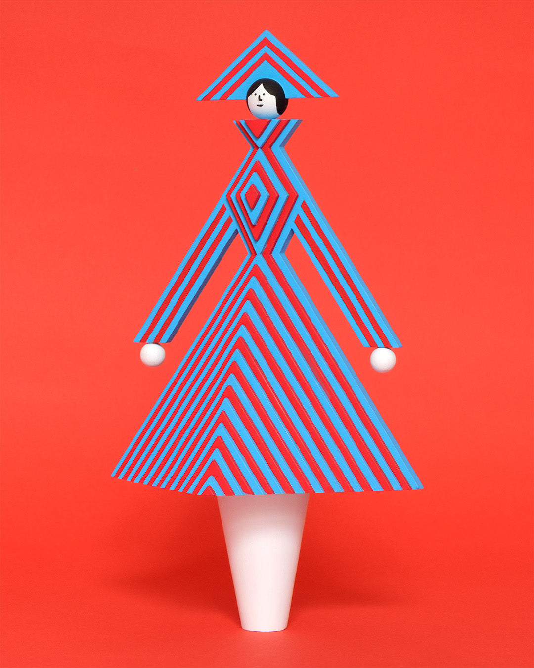 A colourful wooden sculpture with a red and blue stripey 3D top and skirt and a matching headdress with white legs on a plain orange background.