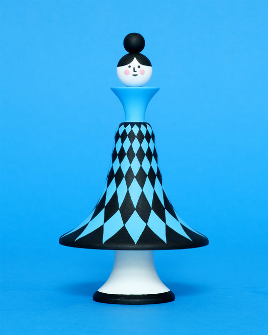 A colourful sculpture with a black and blue diamond patterned curved body with white legs on a plain blue background.