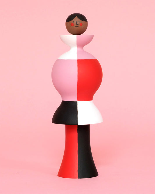 A colourful sculpture with a white, red, black and pink stripey body with red and black legs on a plain pink background.